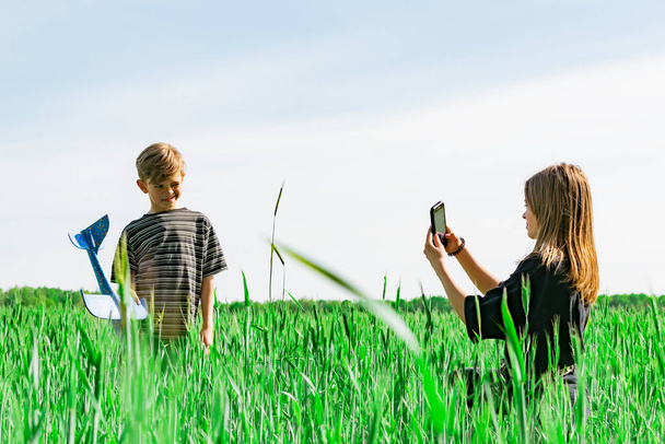 A young girl photographs her younger brother on the field - Foto, imagen