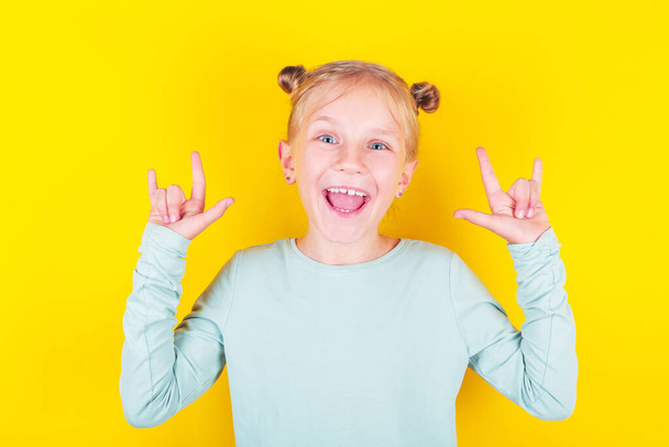 счастливая блондинка, маленькая девочка, делающая знак рок-н-ролла на желтом фоне
.  - Фото, изображение