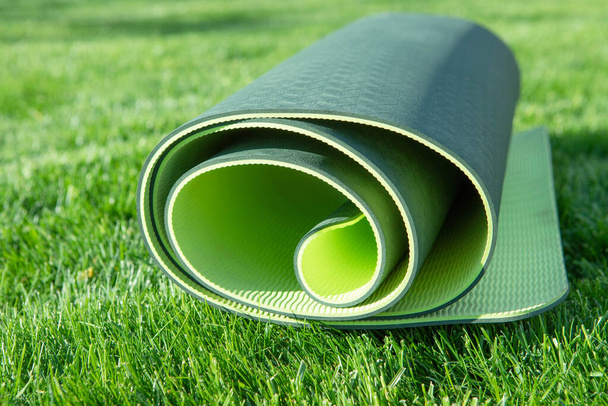 Um tapete de ioga verde fica ligeiramente enrolada em um gramado fresco e grosso. Dia ensolarado. O conceito de estilo de vida, saúde, fitness em casa, fora, atividade em quarentena. Ninguém.
. - Foto, Imagem