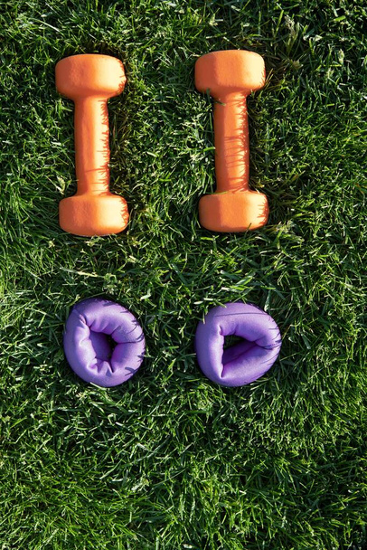 Dumbbells and weights on a green lawn. Bright colors. Orange, purple. Top view. Grass. Concept fitness outside, healthy lifestyle, quarantine, home gym. weight control. Copy space. - Photo, Image