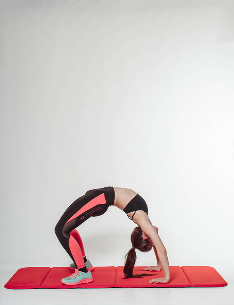 Athletic young woman doing exercise backbend indoor, light background. - Foto, Imagen