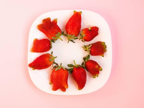 Потворна їжа: незвичайна полуниця в тарілці на рожевому фоні
. - Фото, зображення