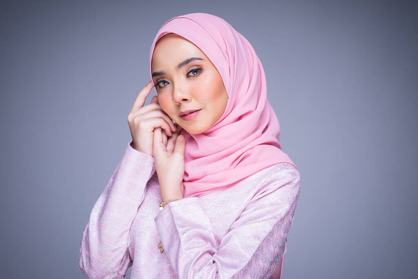 Headshot portrait of a beautiful female model wearing traditional dress and hijab, a lifestyle apparel for Muslim women isolated on grey background. Idul Fitri and hijab fashion concept. - Photo, Image