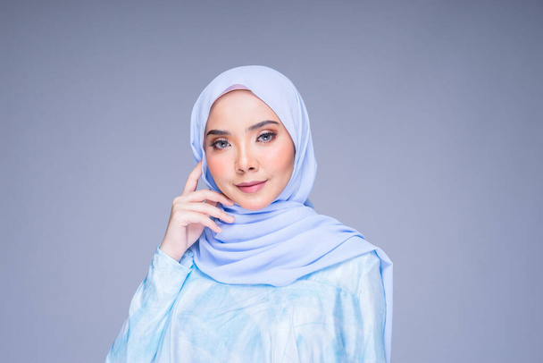 Πορτραίτο κεφαλής ενός όμορφου γυναικείου μοντέλου που φορά παραδοσιακό φόρεμα και χιτζάμπ, ένα ένδυμα τρόπου ζωής για μουσουλμάνες γυναίκες απομονωμένες σε γκρι φόντο. Idul Fitri και χιτζάμπ έννοια μόδας. - Φωτογραφία, εικόνα