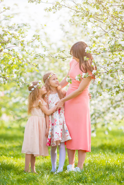 Adorable little girls with young mother in blooming cherry garden on beautiful spring day - Photo, image