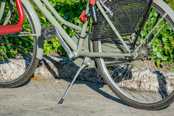 A gray bike with red trim stands on a backup on the sidewalk. Bicycle pedals close up. - Photo, image