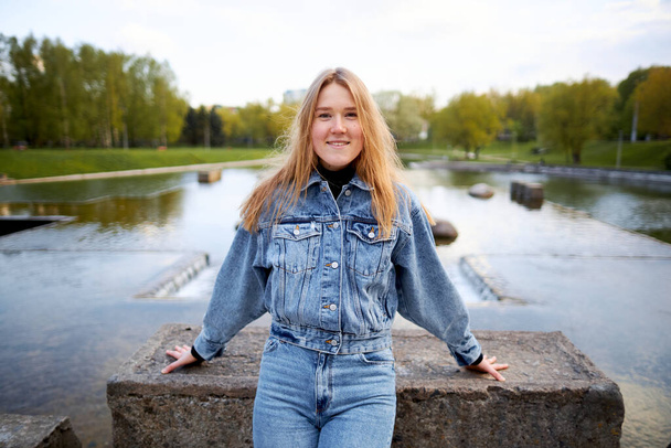 Beautiful portrait of a 90s redhead scandinavian teenager girl in jeans in a park near a lake. - Zdjęcie, obraz