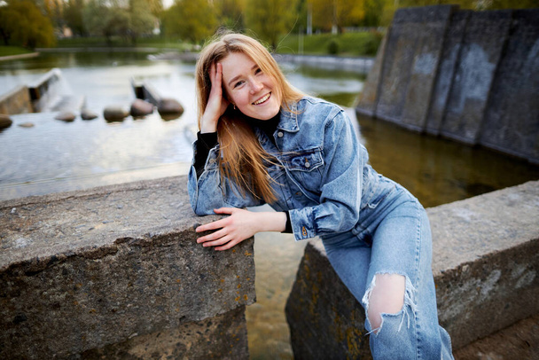 Beautiful portrait of a 90s redhead scandinavian teenager girl in jeans in a park near a lake. - Foto, afbeelding