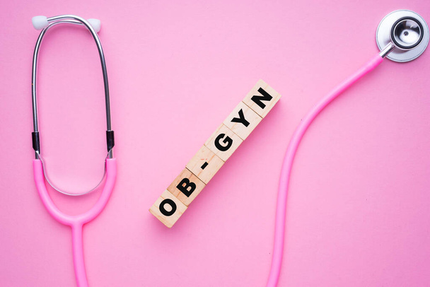 Frauen im Gesundheitswesen. Ein rosafarbenes Strethoskop auf rosa Hintergrund mit Holzblock-Schreibweise Ü-GYN oder Geburtshilfe und Gynäkologie - Foto, Bild