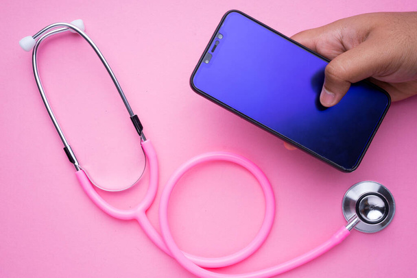 Tecnología en el concepto de salud de las mujeres. Un estetoscopio rosa y un smartphone sobre fondo rosa. Orientación al paisaje
. - Foto, imagen