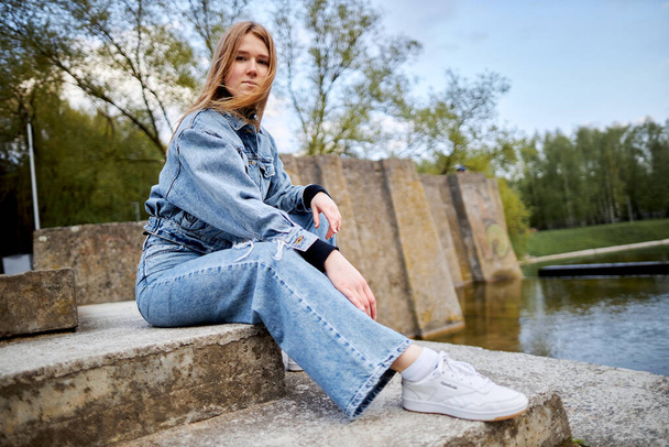 Beautiful portrait of a 90s redhead scandinavian teenager girl in jeans in a park near a lake. - Фото, изображение