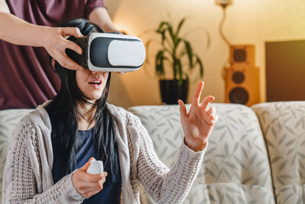 Young beautiful girl with long hair wearing VR glasses with friend help - Photo, image
