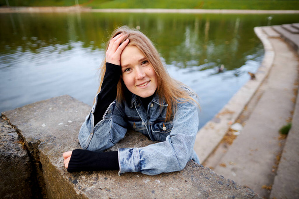 Schöne Nahaufnahme Porträt eines rothaarigen Teenagers in Jeans der 90er Jahre in einem Park in der Nähe eines Sees. - Foto, Bild