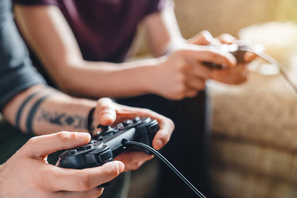 Close up of unrecognizable friends in casual clothing using joysticks while having fun with video game at home - Foto, Imagen