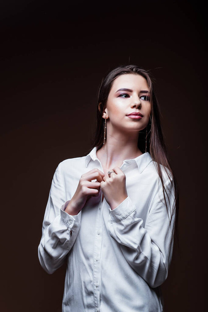 Beauty. Femininity. Beautiful female face with perfect genuine skin. Beauty salon. Make-up artist. Portrait of a beautiful woman in the studio. The girl inflates her hair. Girl in a white shirt. Face. - Foto, afbeelding