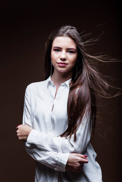 Beauty. Femininity. Beautiful female face with perfect genuine skin. Beauty salon. Make-up artist. Portrait of a beautiful woman in the studio. The girl inflates her hair. Girl in a white shirt. Face. - Foto, imagen