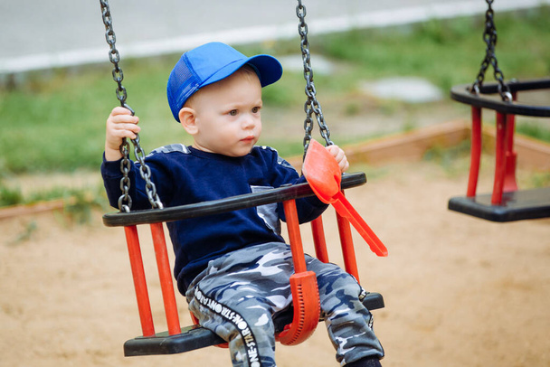 Beautiful child riding a swing and holding toys in his hands - Foto, Bild