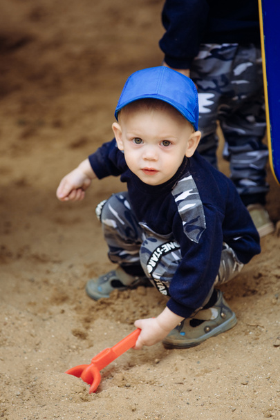 A boy plays in the playground with sand and holds a shovel - Φωτογραφία, εικόνα