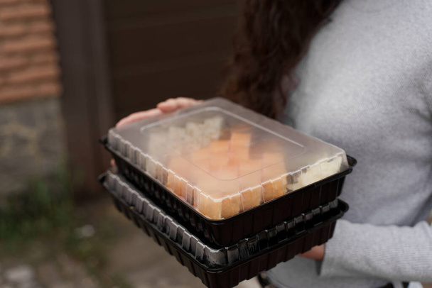 Суши крупным планом поставляются в коробке здоровой доставкой продуктов питания онлайн. Девушка держит в руках 2 набора суши. Японская кухня: булочки, соевый соус, васаби. Объявления для ресторана 1 + 1
 - Фото, изображение