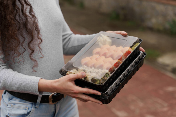 Primo piano sushi in scatola di cibo sano consegna servizio online. Ragazza tiene 2 set di sushi in mano. Cucina giapponese: panini, salsa di soia, wasabi. 1 + 1 annuncio per ristorante
 - Foto, immagini