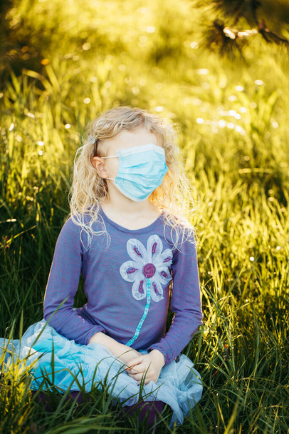 Young girl in sanitary face mask covering her face. Child wearing protective mask against coronavirus outdoor. Concept of panic, safety and health protection during covid-19 quarantine. - Photo, Image
