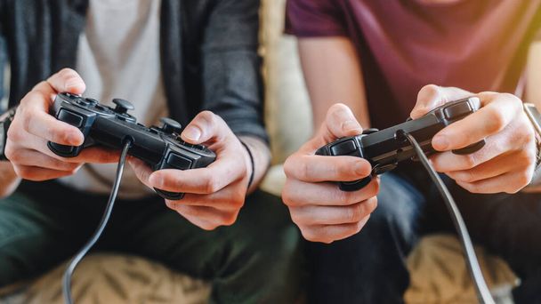 Cropped image of young men playing video games while sitting on sofa at home - Fotó, kép