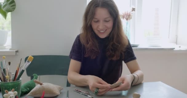 Žena vyrábějící keramickou část pro panenky. Žena sedí a vytváří ucho pro panenku doma u stolu. Části hrnčířských panenek, ruční práce a kreativní dovednosti - Záběry, video