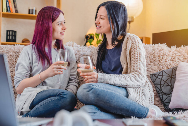 Cheerful young female friends with wine glasses on sofa at home - Foto, immagini