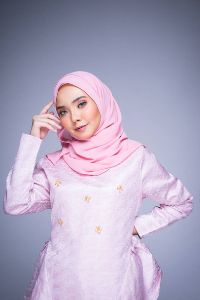 Half length portrait of a beautiful female model wearing traditional dress and hijab, a lifestyle apparel for Muslim women isolated on grey background. Idul Fitri and hijab fashion concept. - Photo, Image