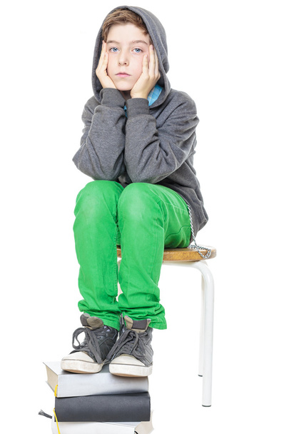έφηβο αγόρι κάθεται σε ένα σκαμνί, με τα πόδια του σε μια στοίβα του βιβλίου - Φωτογραφία, εικόνα