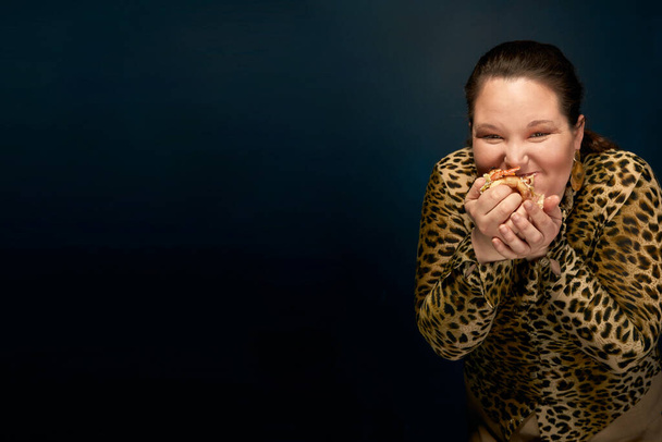 Overweight girl in a leopard blouse with a hamburger in her hand - Foto, imagen