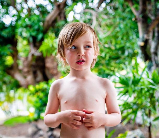 Jonge jongen trekt een grappig gezicht buiten in groen blad. Locatie Hawaï. - Foto, afbeelding