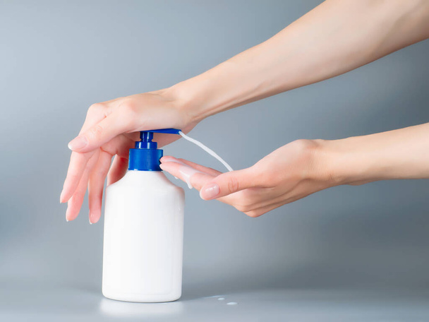 Woman hands pouring liquid soap from dispenser. On gray background - Foto, afbeelding