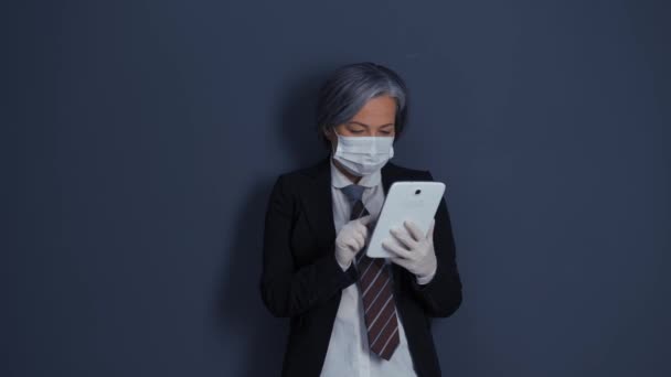 Businesswoman with grey hair in protective mask and gloves holding and looking at tablet standing in business suit. Health care concept. Business concept. Prores 422 - Кадри, відео