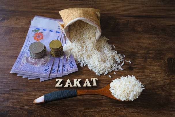 Palabra ZAKAT, dinero, moneda apilada, y arroz sobre fondo de madera .Zakat Concept. Zakat es el reparto de la riqueza de los ricos para los menos afortunados
. - Foto, imagen