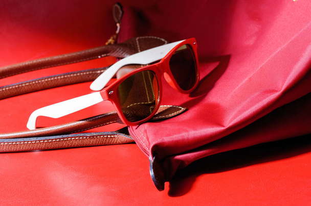Женский аксессуар, крупный план красные пластиковые солнцезащитные очки на красном фоне
 - Фото, изображение