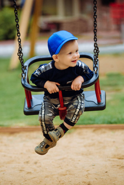 Handsome boy 1-2 years old, sitting on a swing, playground, close up - Photo, Image