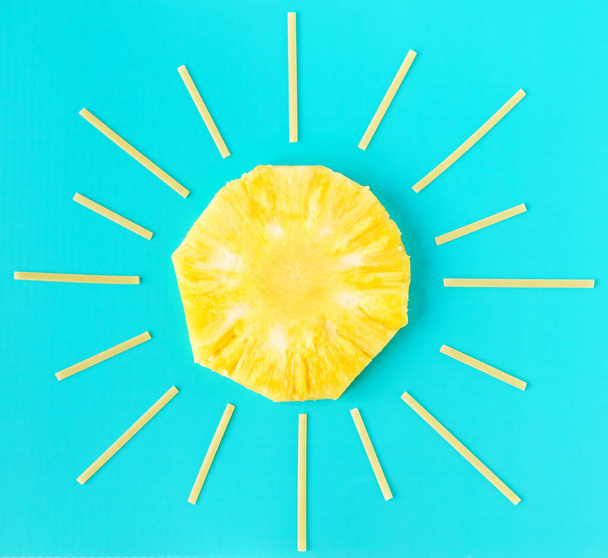 Creatief zomer minimaal concept. Zon gemaakt van gele ananas ronde plak en spaghetti als zonnestralen op helderblauwe achtergrond. Indeling van voedsel en fruit, plat leggen, modelleren - Foto, afbeelding