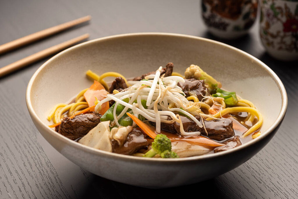 meat tenderloin yakisoba on a bowl - noodles with vegetables with soy sauce on a blurred background - Zdjęcie, obraz