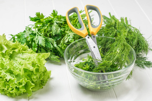 A bowl of chopped salad greens and scissors on a white table. - Photo, Image