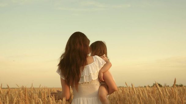 Anya búzával sétál a mezőn. Egy földműves nő egy gyerekkel a mezőn. boldog család, ökoturizmus. egy kisbaba anya karjaiban. Anya és a kislánya játszanak a mezőn érett búza a napon. - Fotó, kép