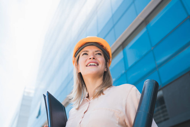 Portrait of professional architect woman wearing yellow helmet and standing outdoors. Engineer and architect concept. - Foto, Imagem