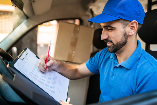 Portrait of a delivery man checking the delivery list while sitting in van. Delivery and shipping concept. - Foto, Bild