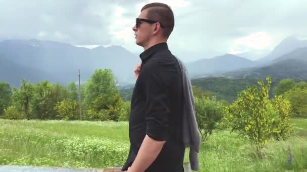 handsome man in sunglasses and casual clothes walking among mountains at summer day   - Footage, Video