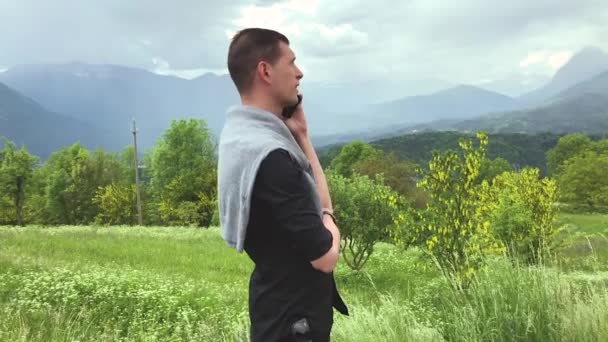 красивий чоловік у повсякденному одязі розмовляє по смартфону під час прогулянки серед гір в літній день
 - Кадри, відео