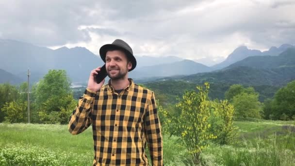 komea mies rento vaatteet puhuu älypuhelimella aikana kävellä vuorilla kesäpäivänä - Materiaali, video