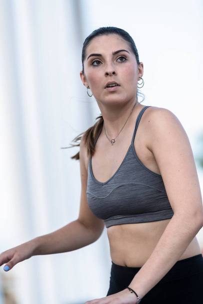 Close up of a beautiful young woman with a grey sports bra and black tights on an out of focus background. Healthy lifestyle concept. - Photo, Image