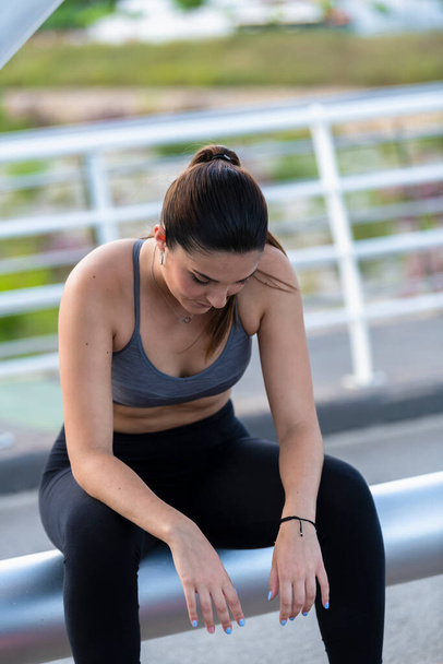 Young woman wearing a grey sports bra and black tights sitting and taking a break on an out of focus background. Healthy lifestyle concept. - 写真・画像