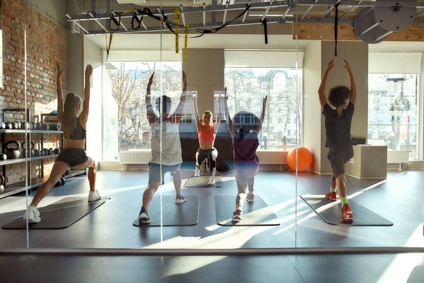Join the world of yoga. Full-length shot of kids doing yoga exercises together with female trainer in gym. Stretching on a sunny day. Sport, healthy life, physical education concept - Foto, imagen