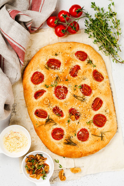 Italian traditional focaccia bread baking with with cherry tomatoes, parmesan and rosemary on light brown background. Top view. - Φωτογραφία, εικόνα